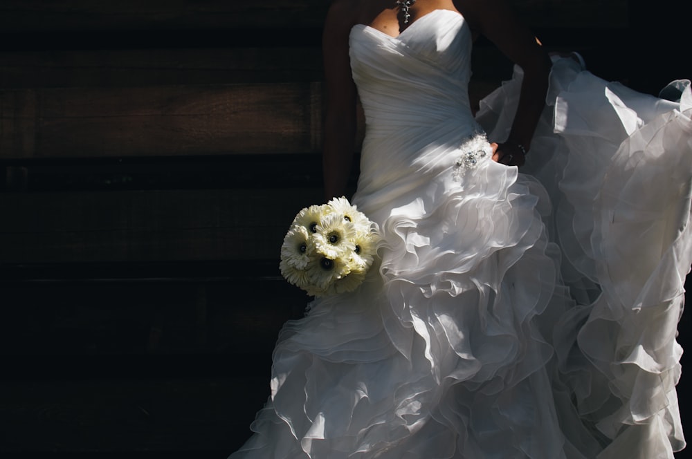 A bride holding her bouquet of daisies wearing a ruffled wedding dress