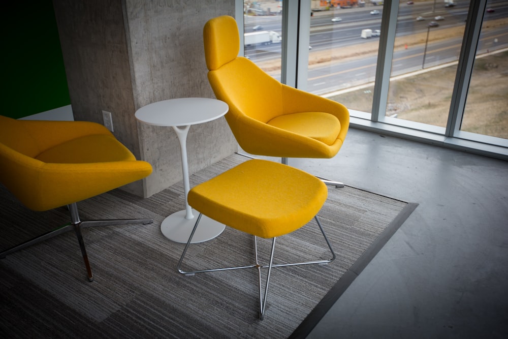 Sala com cadeiras de tecido amarelo e otomana com mesa