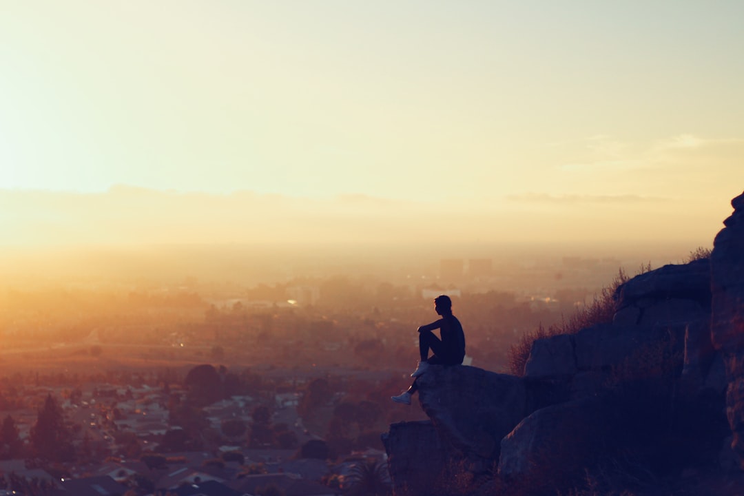 man sitting on rock formation in cliff during golden hours,