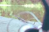 A close-up of a fishing rod and reel set against a calm freshwater lake at dawn.