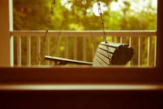 A serene porch setting featuring a SwingNest porch swing with plush Sunbrella cushions under a shaded pergola.