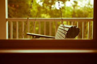 A cozy porch swing hanging gently on a sunny veranda surrounded by lush greenery.