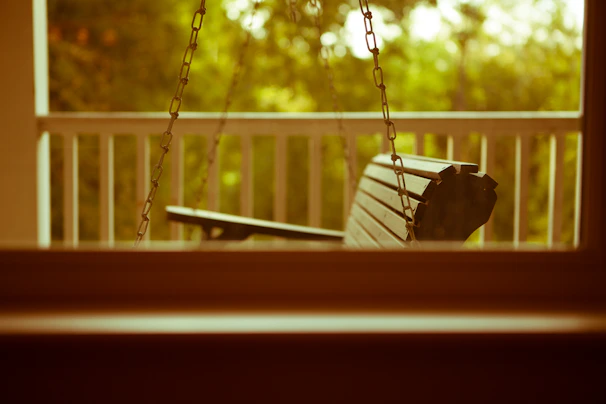 A cozy porch swing hanging gently on a sunny veranda surrounded by lush greenery.