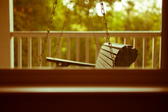 A serene porch setting featuring a SwingNest porch swing with plush Sunbrella cushions under a shaded pergola.