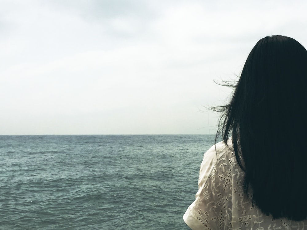 woman facing body of water under cloudy sky