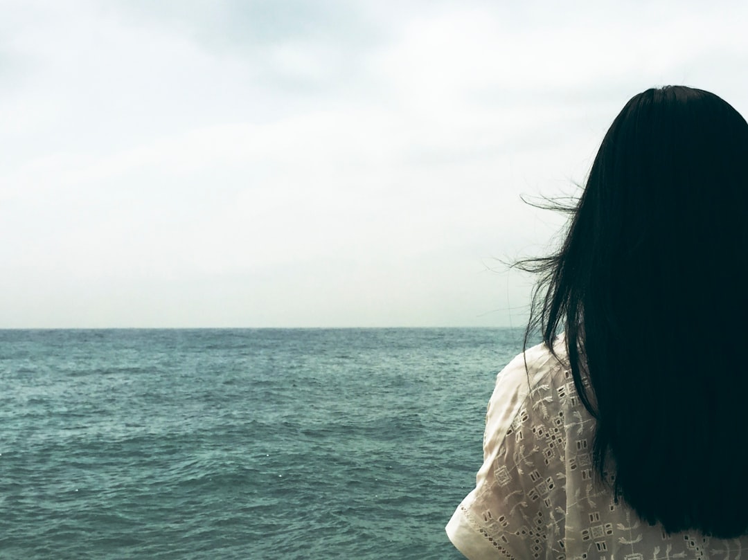 woman facing body of water under cloudy sky