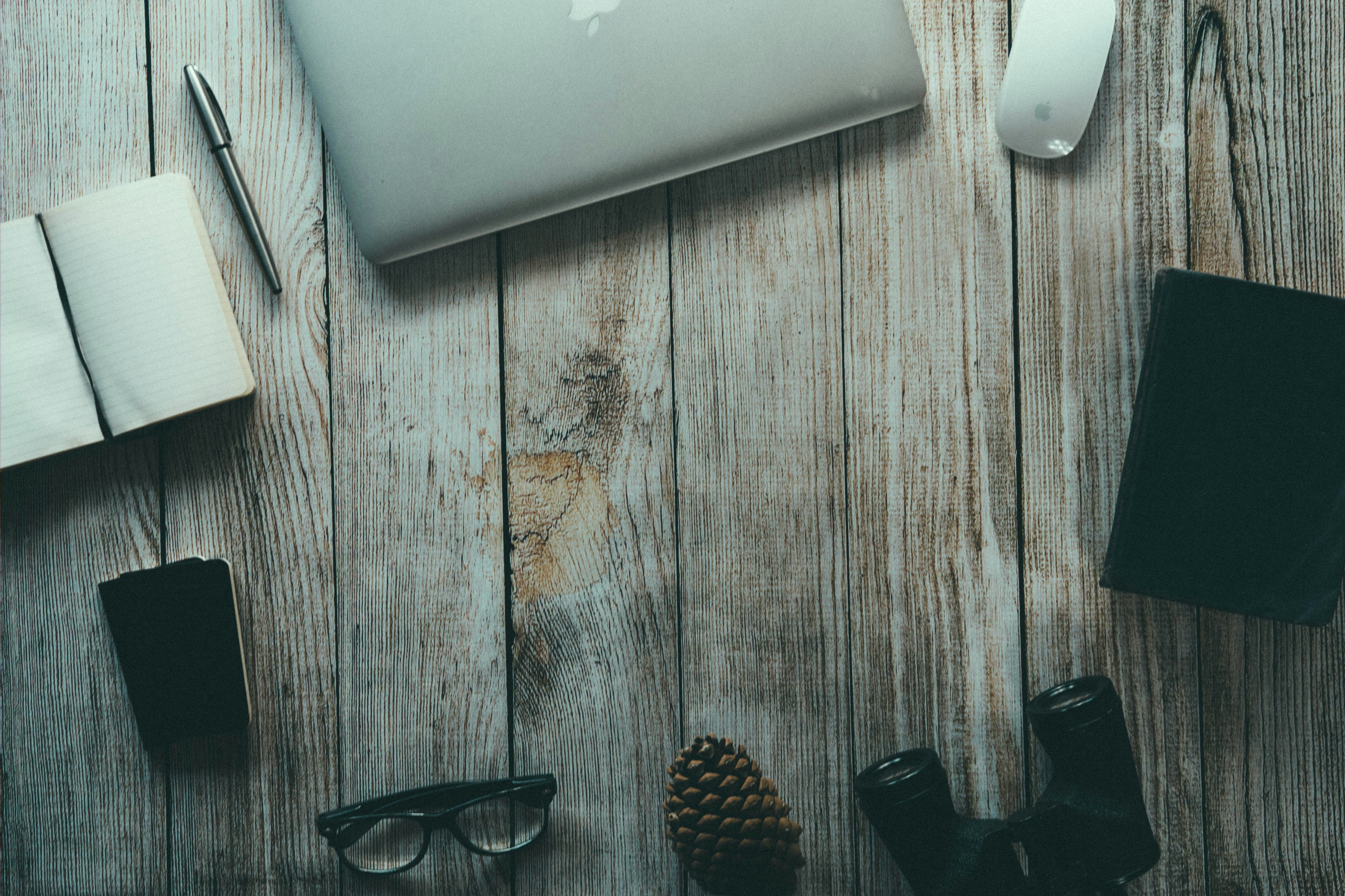 silver MacBook, ballpoint pen, binoculars, eyeglasses arranged in circular pattern