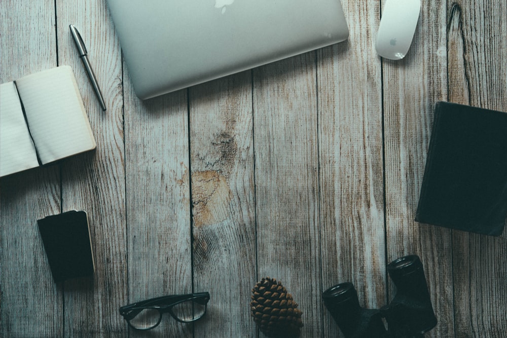 silver MacBook, ballpoint pen, binoculars, eyeglasses arranged in circular pattern