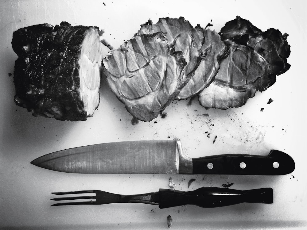 Foto en escala de grises de carne a la parrilla junto a cuchillo y tenedor
