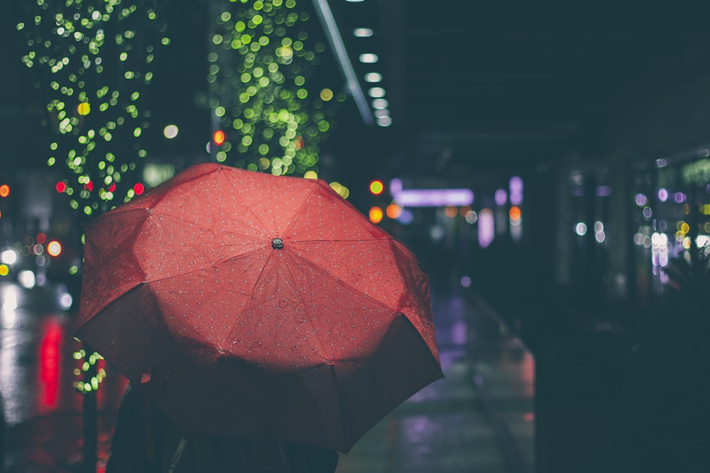 빨간 우산을 쓴 사람이 밤에 거리를 걷고 있습니다.