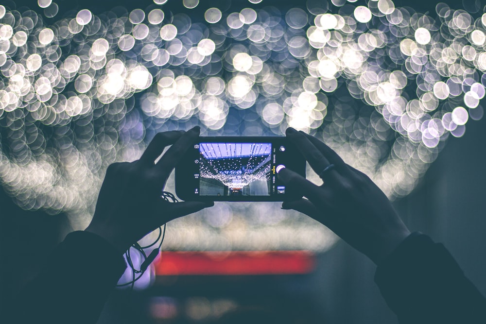 selective focus photography of person holding smartphone while taking picture of scenery