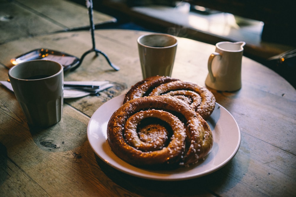 plate of glazed bread near mugs on tabletop