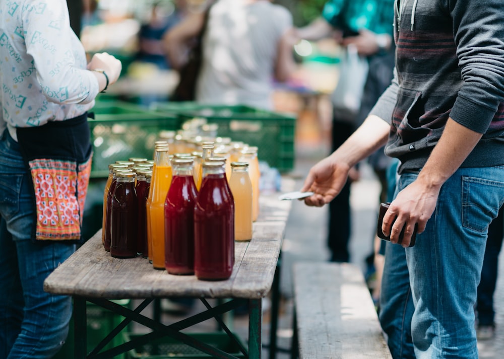 person holding clear glass jar with red liquid