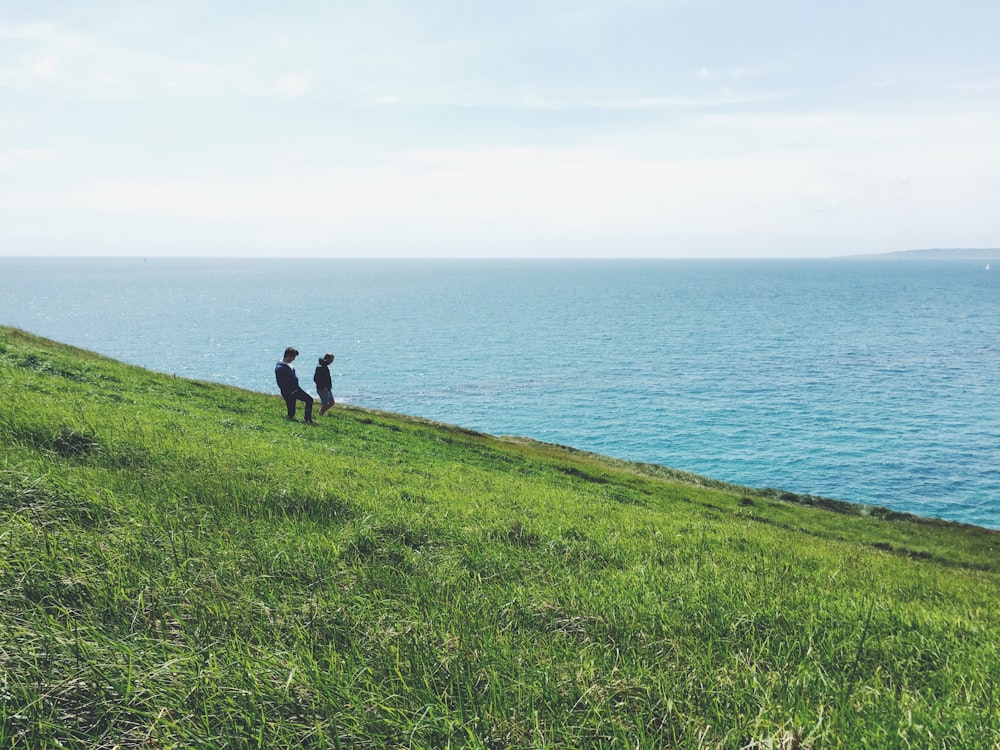 Dos personas de pie en la hierba verde frente al océano