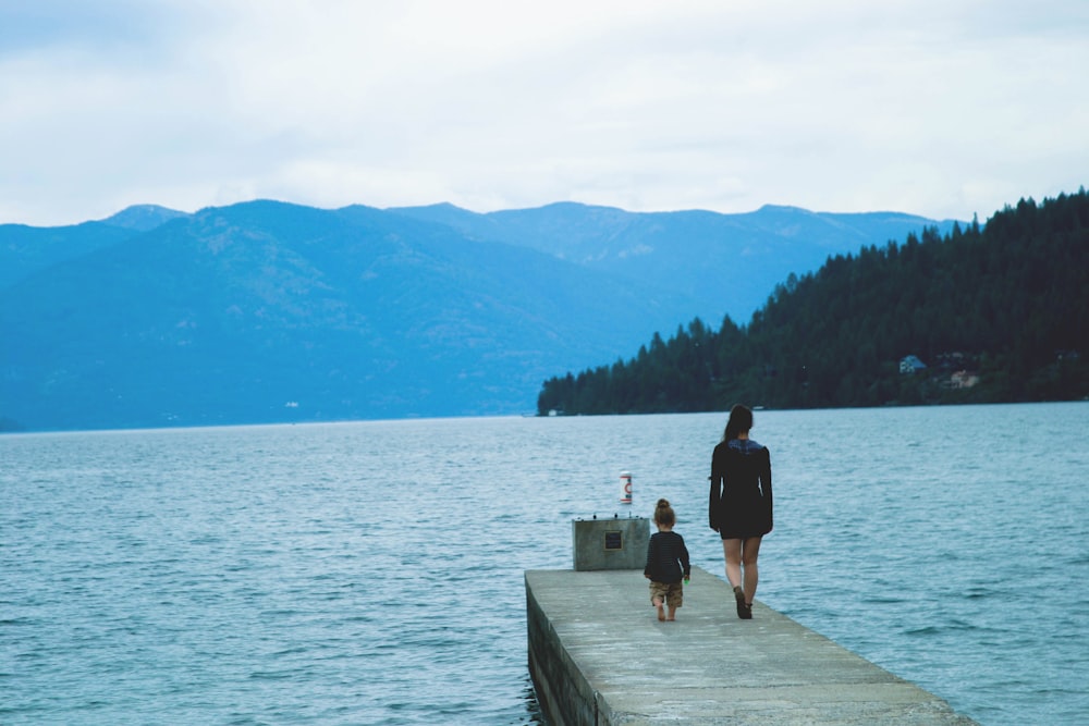 femme et fille marchant le long du quai en béton entouré par le plan d’eau