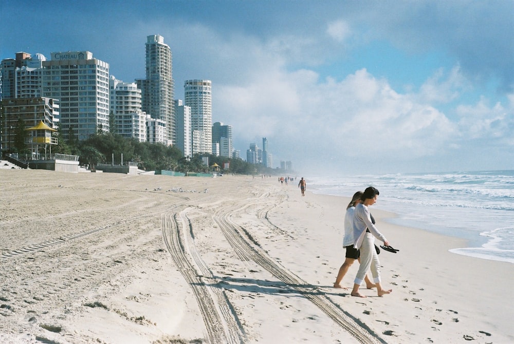 낮에 콘크리트 건물 근처의 해변을 걷는 사람들