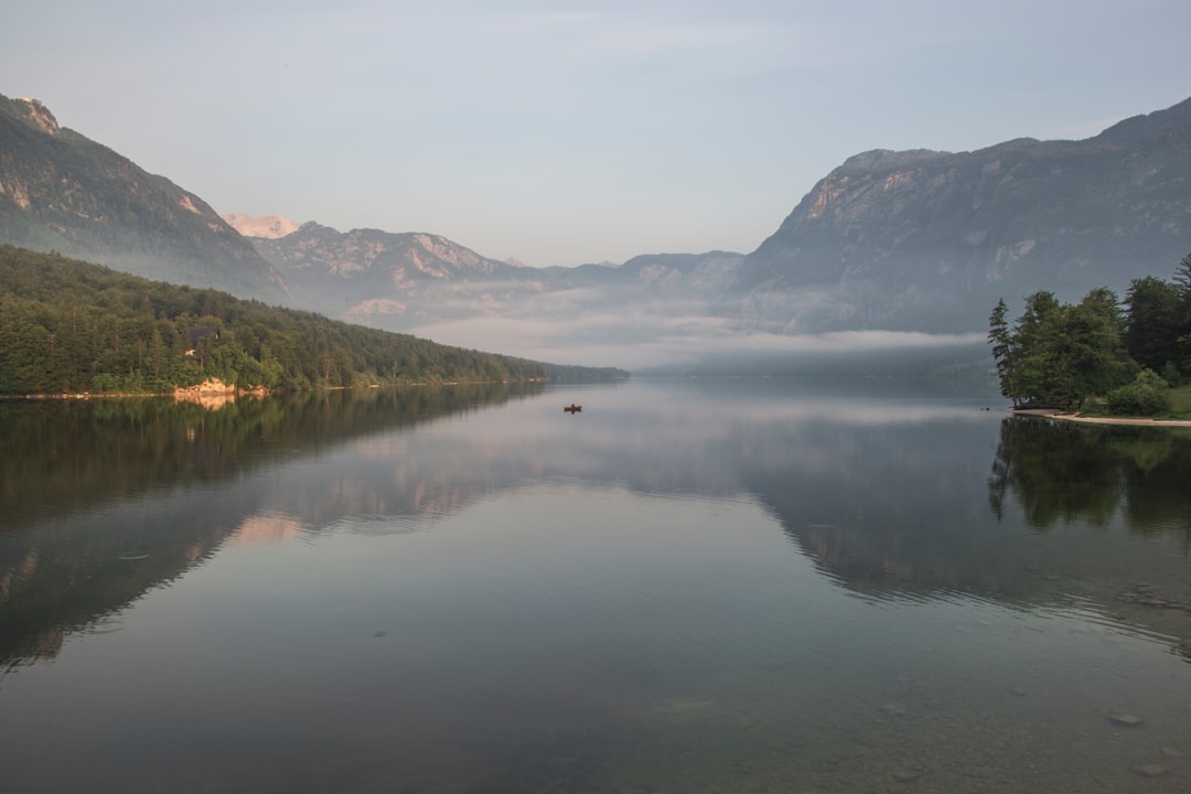 body of water near mountain ranges with green vegetation covered with fog during daytime