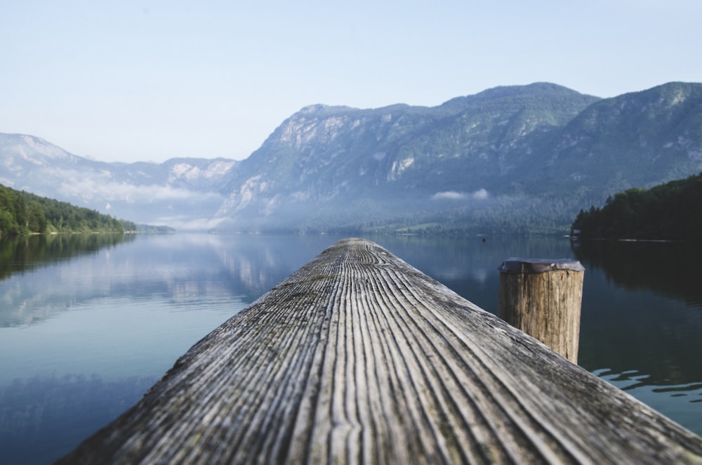 gray wood beam near body of water surrounded by mountain ranges during daytime