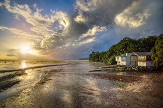 photo of white and brown wooden house beside seashore during sunrise