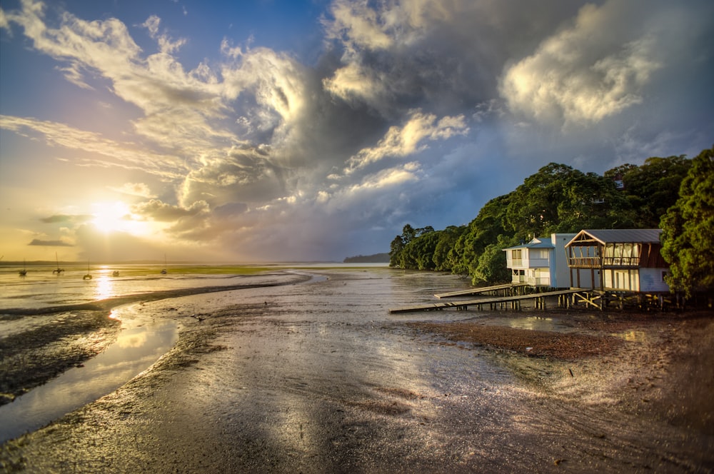 photo of white and brown wooden house beside seashore during sunrise