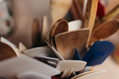 A collection of wooden and silicone kitchen utensils, including spatulas and spoons, is gathered in a container. The mix of materials features both natural wood and colored silicone pieces.