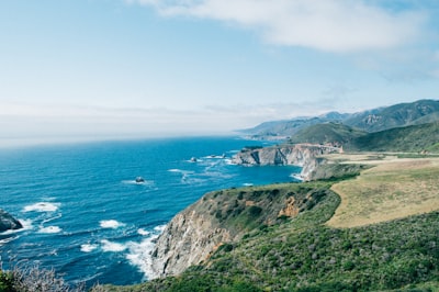 mountain cliff near water under clear sky coast teams background