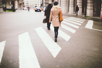Elegant woman in beige coat walking through a sunlit urban street