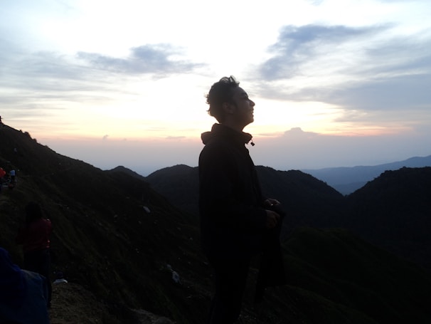 A silhouette of a person meditating on a mountain peak during sunset.