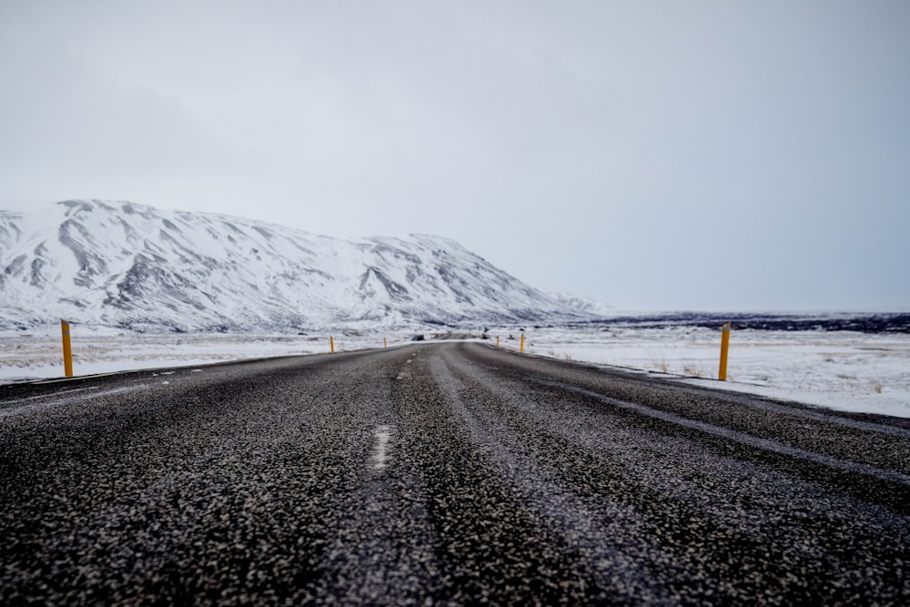 route goudronnée près de la montagne remplie de neige sous un ciel nuageux