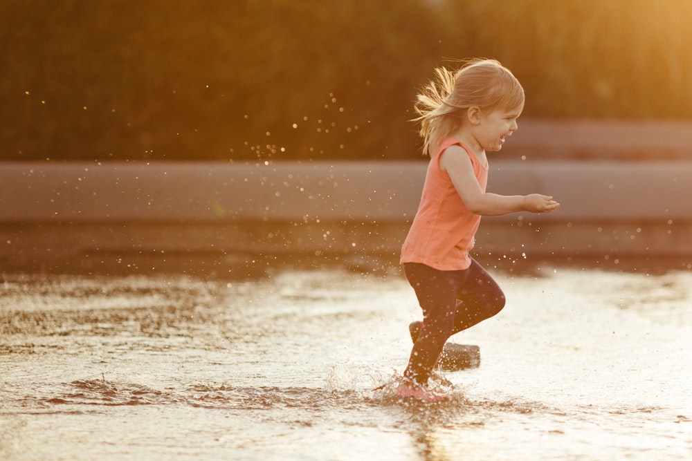 Chica con camiseta sin mangas rosa y pantalones cortos marrones corriendo en el agua durante el día