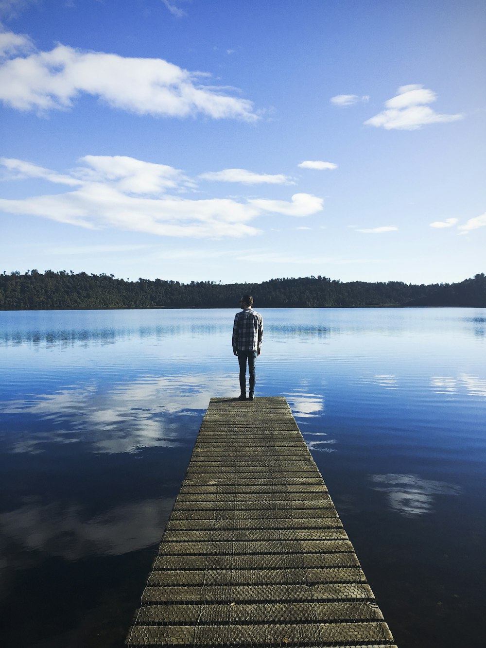 man standing on lake dock watching water under blue sky during daytime