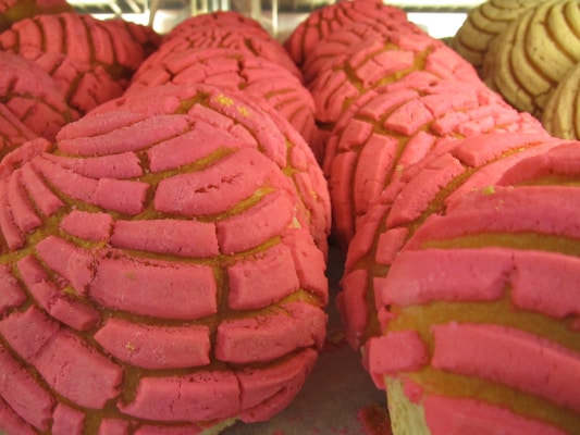 A close-up view of several pieces of Mexican sweet bread known as conchas, featuring a vibrant pink sugar topping with a shell-like design. The soft bread beneath appears golden brown and is partially covered by the sugary crust.