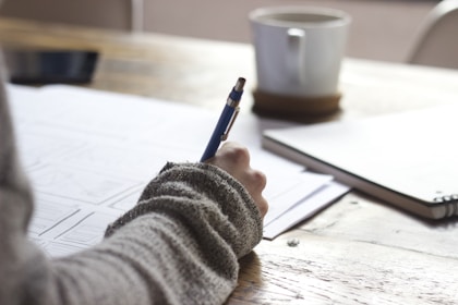 person writing on brown wooden table near white ceramic mug learning Italian