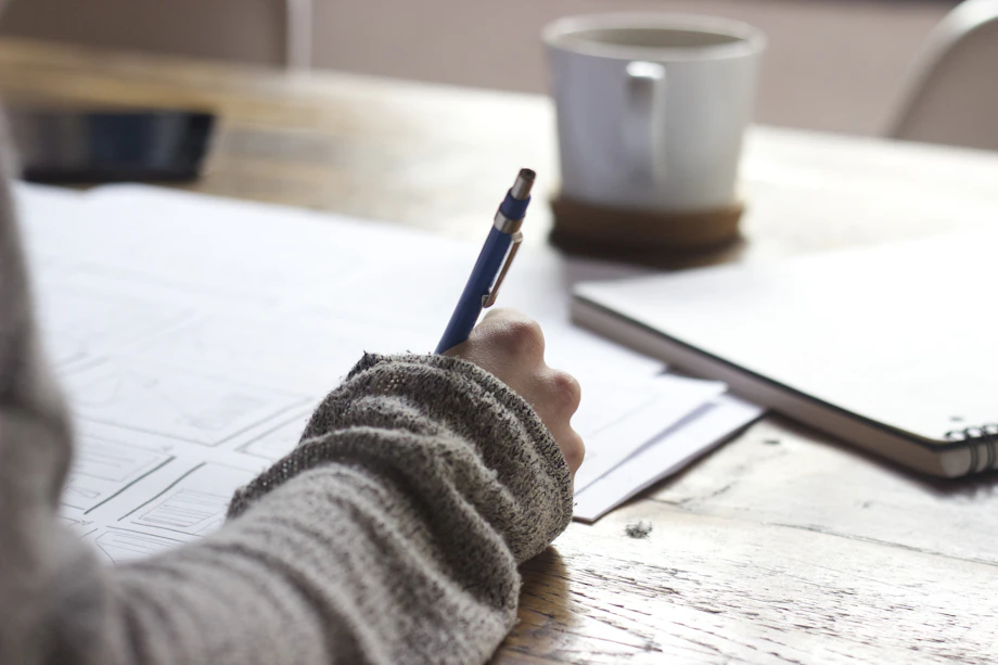 Persona escribiendo en un cuaderno junto a un portátil