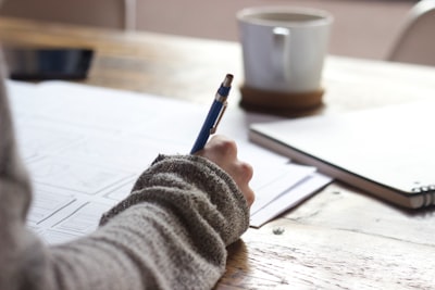 person writing on brown wooden table near white ceramic mug personal zoom background