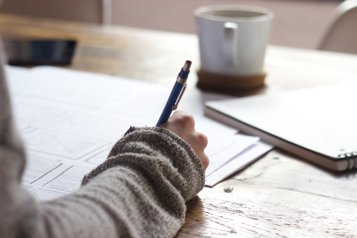 person writing with coffee and notebooks