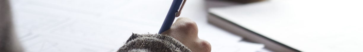 person writing on brown wooden table near white ceramic mug