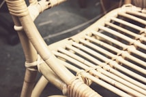 Close-up view of a woven rattan chair with intricate patterns. The chair features natural beige tones with visible texture and a focus on the craftsmanship of the weave.