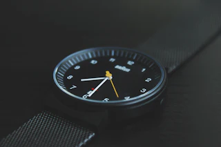 Black Braun wristwatch with white numerals and a yellow second hand on a dark surface