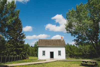 White house with picnic bench and green lawn, blue sky, clouds and trees in Spring