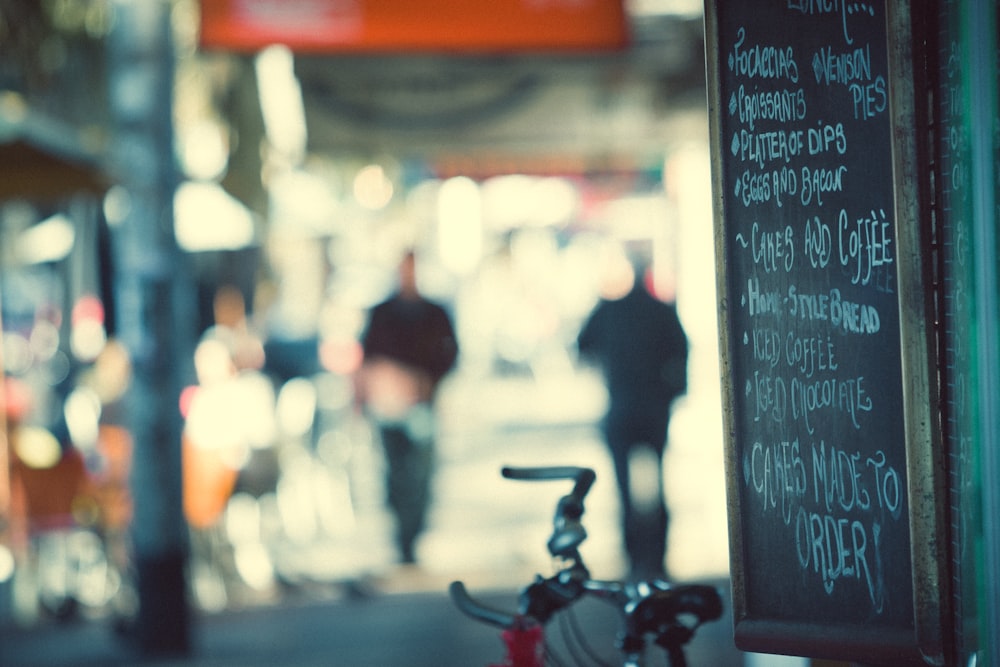 red and gray bicycle parked near black chalkboard with menu writing selective focus photography