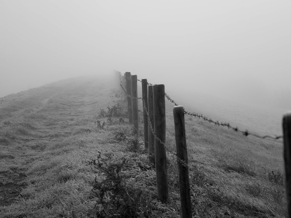 grayscale photo of wooden fence on grass field while fogging
