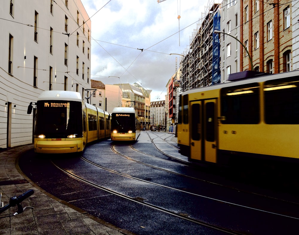 yellow city buses between buildings during daytime