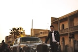 man wearing black suit jacket standing near gray car