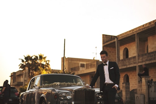 man wearing black suit jacket standing near gray car