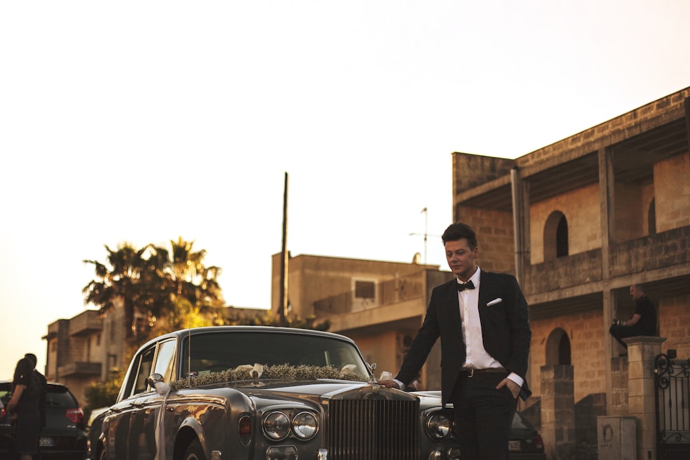 man wearing black suit jacket standing near gray car