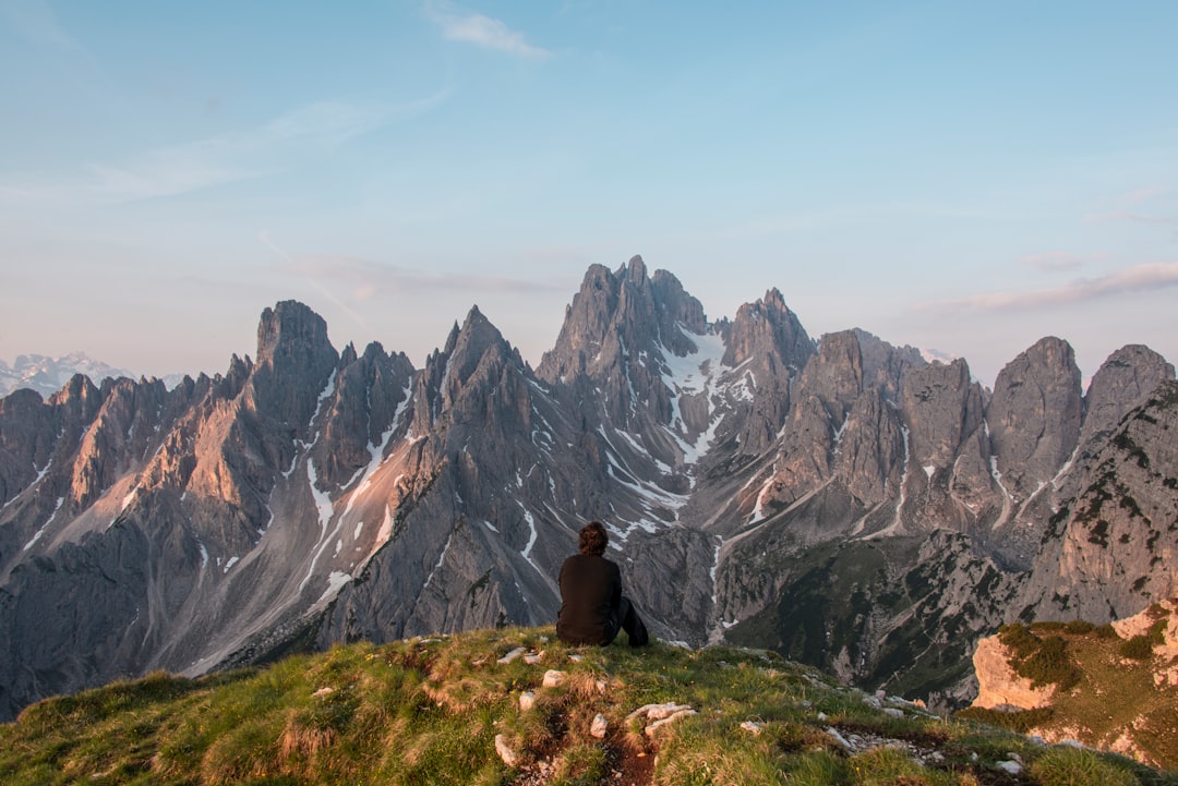 man sitting on cliff facing gray mountain