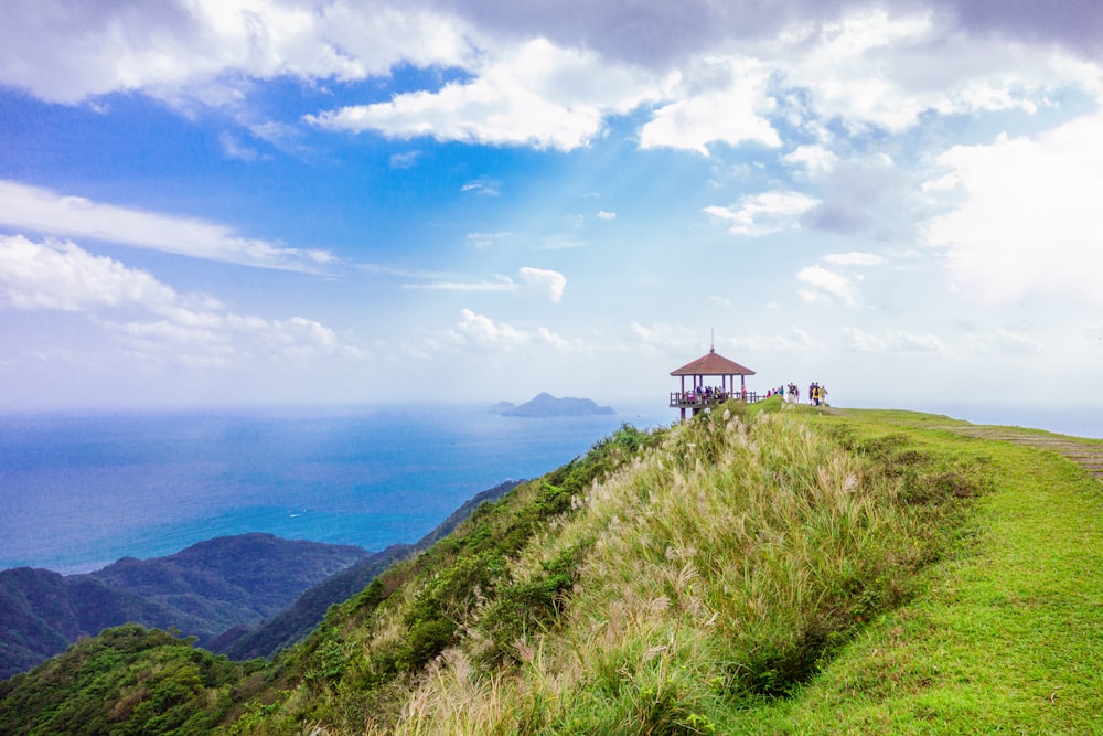 brown gazebo on top of green mountain overlooking sea during daytime landscape photography
