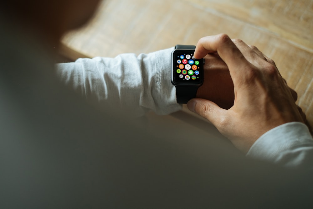 A man in a white sweater wearing and using an Apple Watch with a black band