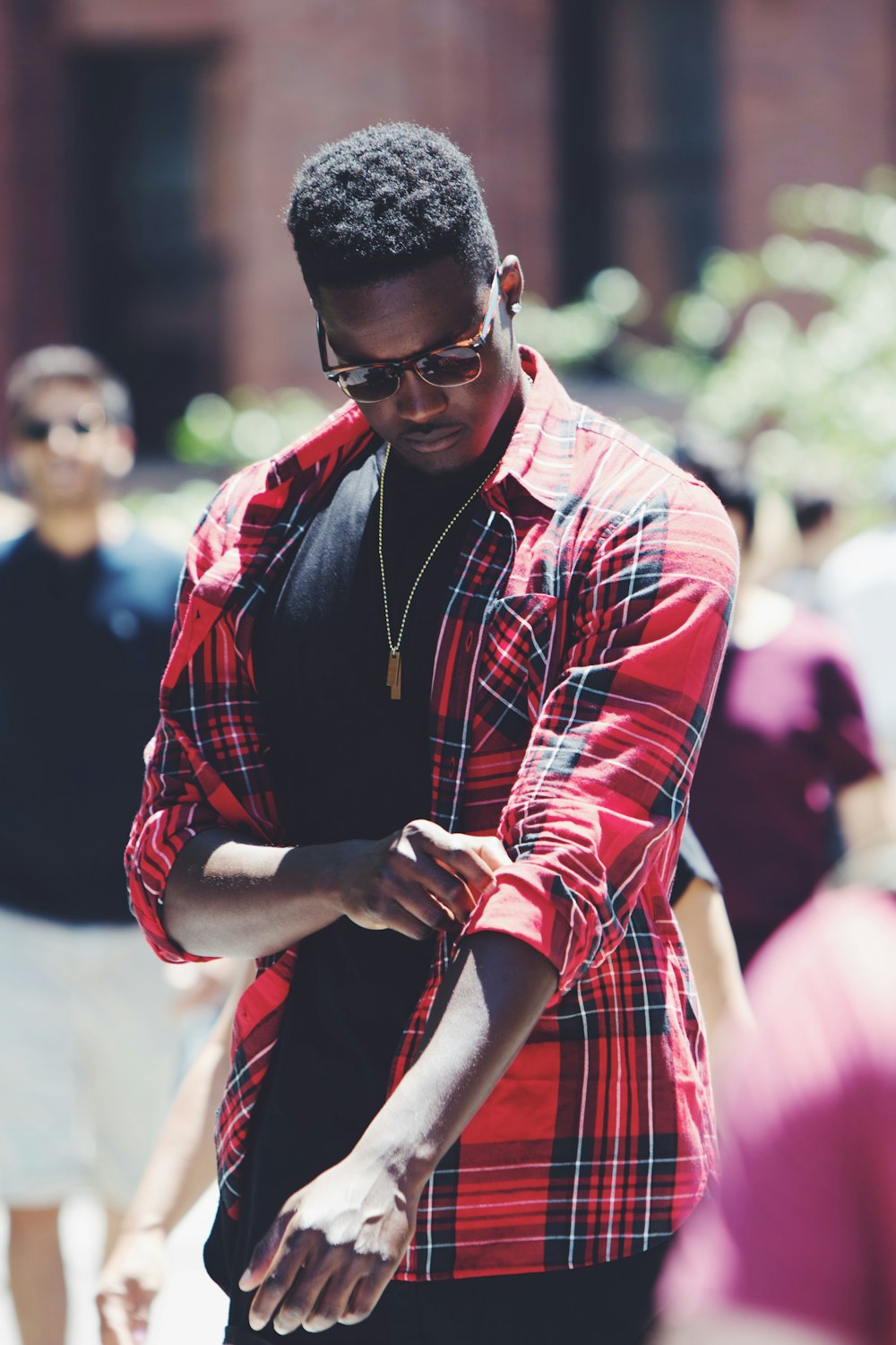 man fixing his red, black, and white plaid sport shirt sleeve during daytime